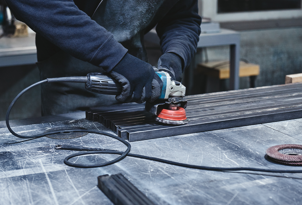 A worker using an angle grinder on metal tubing.